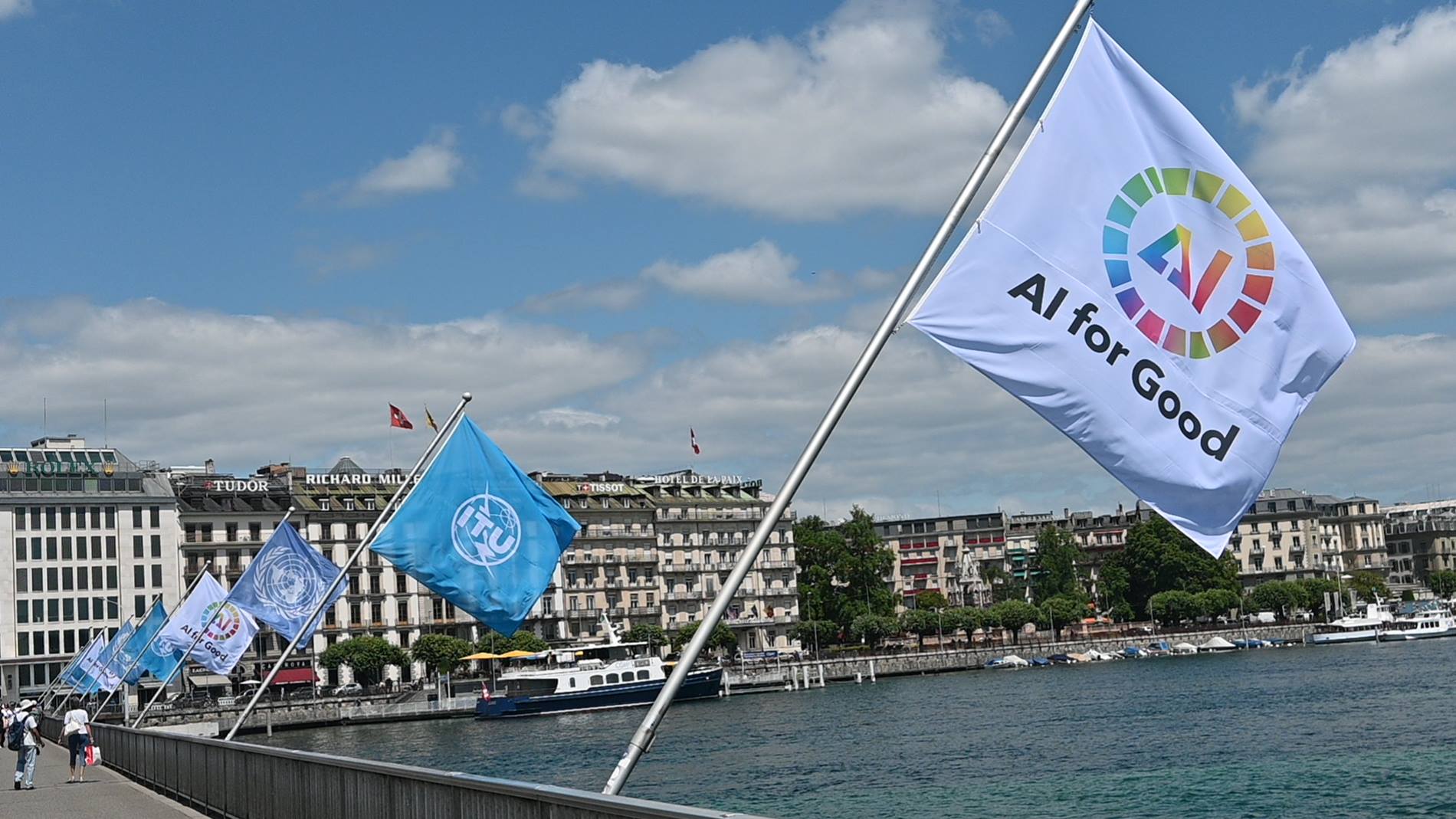 Hình minh hoạ cờ "AI for Good" màu trắng với logo đa sắc phất phới bên bờ hồ Geneva, phía sau là cờ ITU màu xanh và cờ Liên Hợp Quốc, nền kiến trúc thành phố và bầu trời xanh. Tin chính ngày 04/07/2026: Liên Hợp Quốc ra mắt Ủy ban AI for Good toàn cầu tại Geneva, quy tụ lãnh đạo các nước và CEO công nghệ lớn.