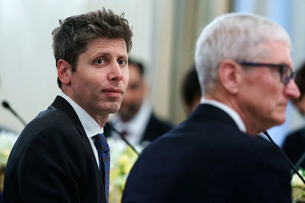Hình minh hoạ cận cảnh Sam Altman, CEO OpenAI, mặc vest đen cà vạt xanh, ánh mắt nhìn sang phía Tim Cook, CEO Apple, đứng phía trước với tóc bạc và kính đen, cả hai đang ngồi dự một sự kiện có micro phía trước. Tin chính ngày 20/07/2026: Apple kiện OpenAI vì cáo buộc đánh cắp bí mật thương mại phần cứng, đặt dấu hỏi cho kế hoạch IPO của OpenAI.